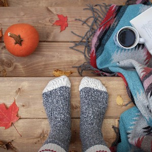 cozy picture of feet on wooden deck with leaves, blanket, coffee, a book and pumpkin